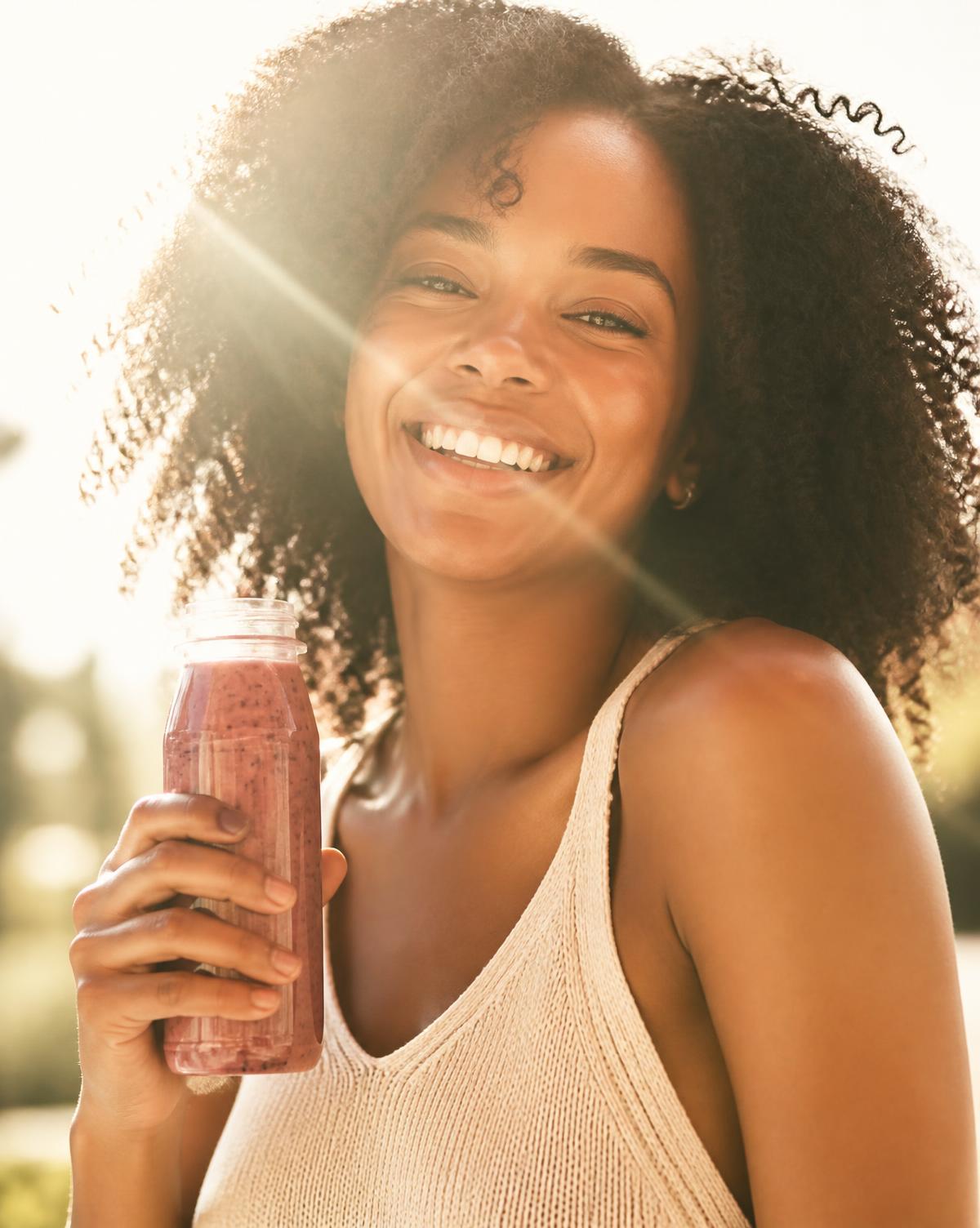 A smiling woman glowing in golden sunlight holding a bottled T4 Smooth smoothie